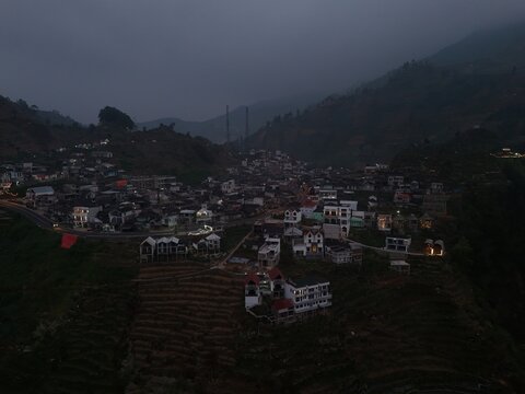 Aerial view of Dieng village nestled in the mountains with terraced fields and winding roads at dusk in Kejajar, Central Java, Indonesia.