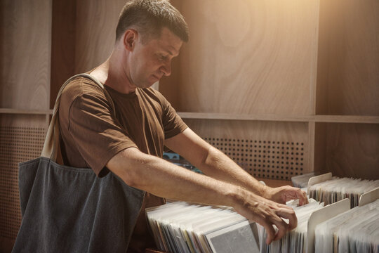 Analog vinyl collector browsing records in music store, man choosing physical media for digital detox, offline leisure, slow living and retro hobby