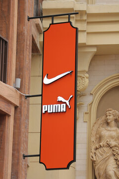 Vertical orange outdoor hanging signboard displaying both Nike swoosh and Puma brand logos at Vinpearl Harbor in Nha Trang, Vietnam on January 27, 2026.