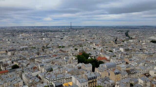 Aerial view of the Eiffel Tower rising above the dense urban landscape of historic Parisian rooftops under a cloudy sky in Paris, Ile-de-France, France.