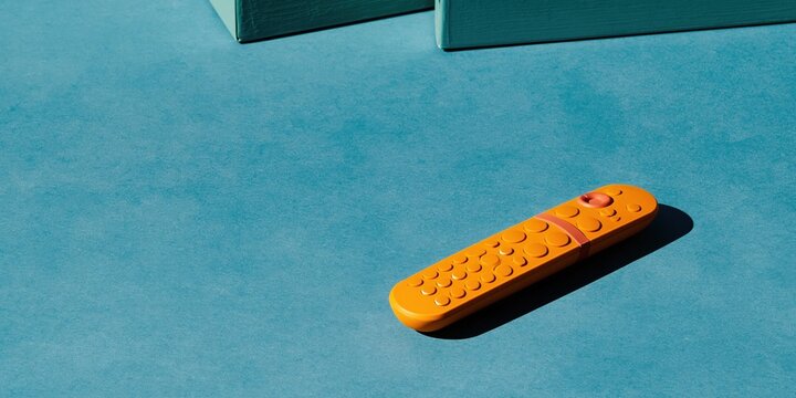 Orange remote control on a vivid blue matte surface with hard shadows and copy space for subscription management