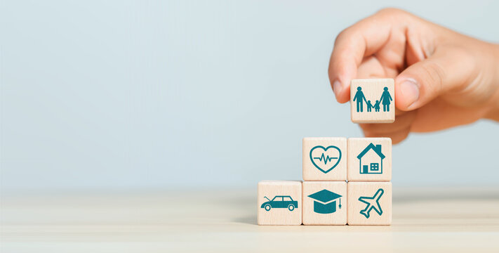 Hand holding a wooden family block above icons for health, home, education, car, and travel, symbolizing family protection, financial planning, insurance, security, and life priorities.