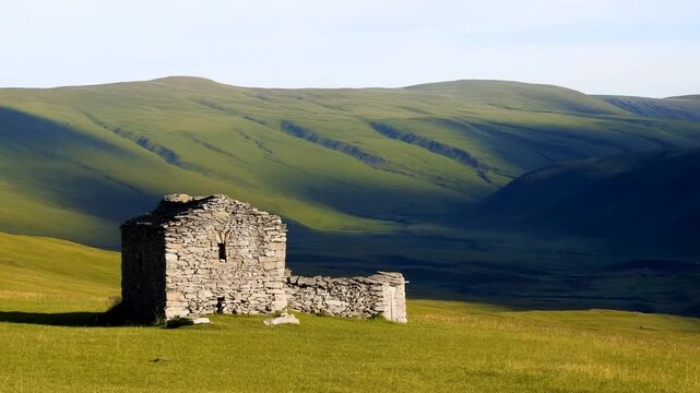 Static shot of stone shelter standing on grassy hillside overlooking rolling green valley and shadowed moorland in remote upland countryside afternoon