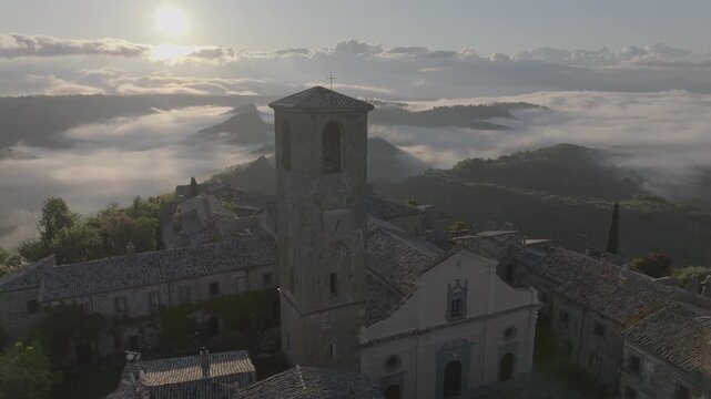 Aerial view of the historic town of Civita di Bagnoregio with its stone church tower rising above the morning mist and rolling hills in Civita di Bagnoregio, Lazio, Italy.