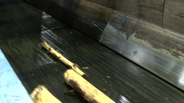 Wood logs being transported on a heavy-duty industrial conveyor inside a timber or pulp processing facility. The machinery moves raw wood for further processing. Waste paper recycling plant