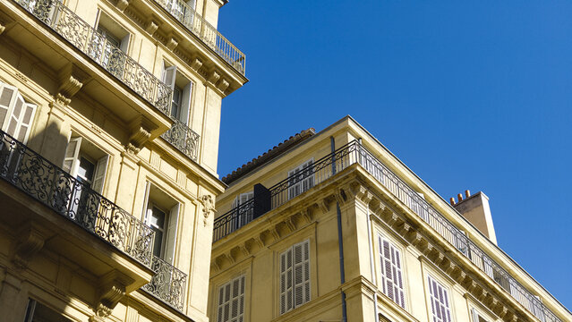 Facades of traditional French buildings with balconies and shutters against a clear blue sky