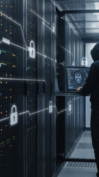 Hooded person typing on laptop connected to secure server rack