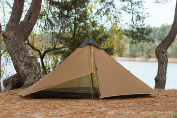 Pyramid tipis camping tent set up in pine forest near lake. Outdoor wilderness survival, bushcraft shelter, ultralight trekking equipment, forest camping and nature adventure travel concept. © vadish