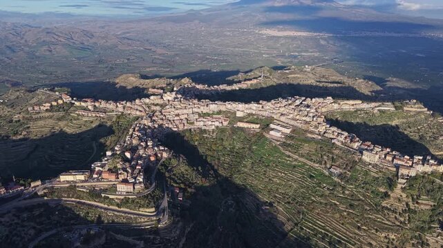 Aerial view of the historic town of Centuripe perched on a mountain ridge surrounded by terraced hills and Mount Etna in the distance, Centuripe, Sicily, Italy.