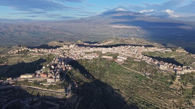 Aerial view of the town of Centuripe shaped like a human figure with Mount Etna in the background and surrounding agricultural terraces in Centuripe, Sicily, Italy.