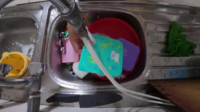 POV view of a man washing dirty plates in a kitchen sink. Hands scrubbing dishes under running water during daily household chores. Concept of home routine, cleanliness, and domestic lifestyle.