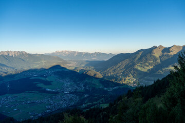 Fototapeta premium Panoramic high-angle view over the valley and surrounding Alpine mountain ranges in clear early morning light, captured from the slopes of Hoher Fraßen in Vorarlberg, Austria
