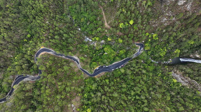 Aerial view of the winding Carretera al Salto de Aguas Blancas road surrounded by dense green forest and a waterfall in Constanza, La Vega, Dominican Republic.