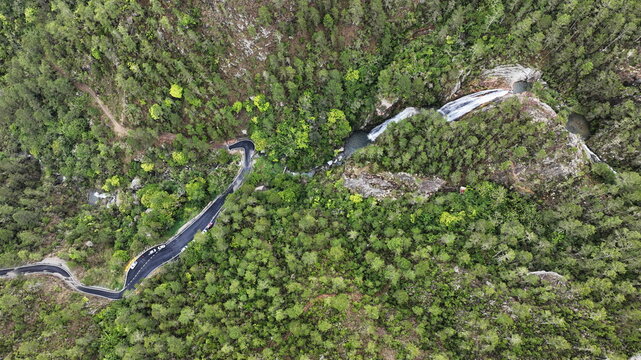 Aerial view of Carretera al Salto de Aguas Blancas winding through the lush green forest and mountainous landscape near the waterfall in Constanza, La Vega, Dominican Republic.