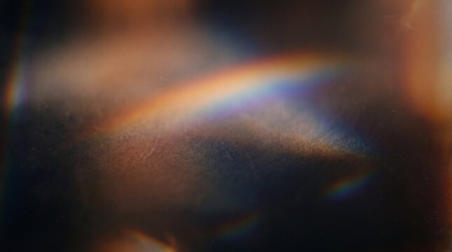 A beautiful abstract background featuring a soft rainbow light leak and prism flare on a dark, textured surface, perfect for creative design projects.