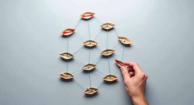 Hand connecting paper boats with blue string on grey background