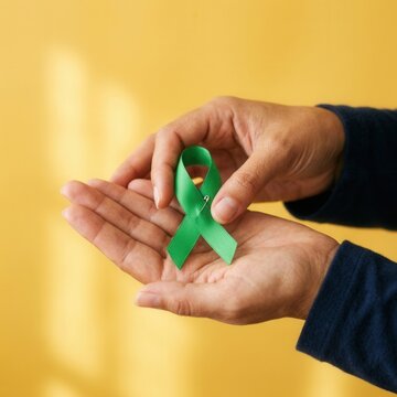 Hand holding green awareness ribbon symbol of hope and support for various causes and charities