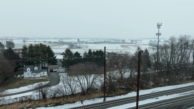 The camera shows a snowy landscape with a winding road in the foreground. Trees and fields appear in the background. The weather is cloudy, creating a gray atmosphere.