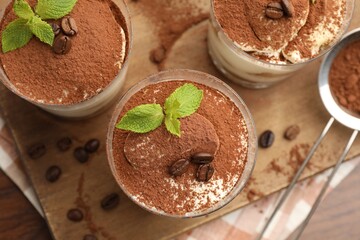 Fototapeta premium Tasty tiramisu with coffee beans and mint in glasses served on wooden table, flat lay