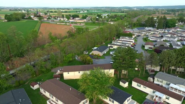 Aerial views show a residential area with mobile, manufactured homes arranged in rows. Green fields and an Amtrak train passes surround the neighborhood,