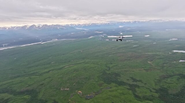 ALASKA - 9.3.2026 - Terrific aerial footage of a bush pilot flying over a lush green valley towards snow-capped Alaska mountains.