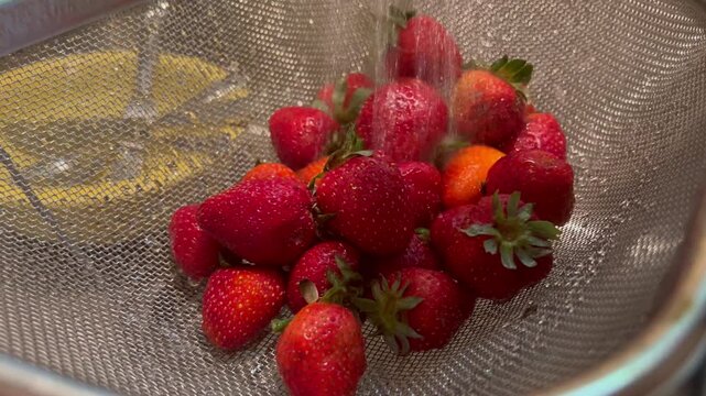 Washing fresh strawberries in mesh colander under running tap water