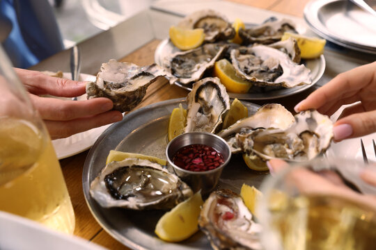 Women eating delicious oysters at wooden table, closeup