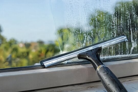 Window squeegee resting on sill with half cleaned soapy glass