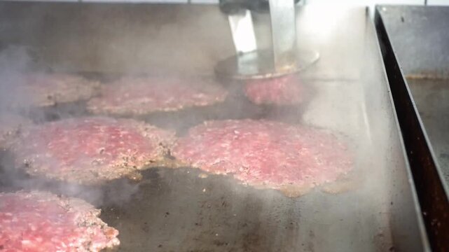 Close up of burger press smashing a beef patty on a hot griddle