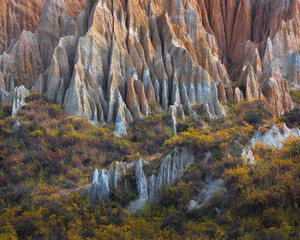 Layered eroded rock spires rise above colorful vegetation, creating a rugged geological landscape ideal for nature, travel, erosion and dramatic terrain themes. © UQink
