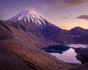 Snow-capped volcanic peak rises above a dark crater lake beneath a soft purple sky, creating a dramatic alpine landscape ideal for travel, adventure and wilderness themes. © UQink
