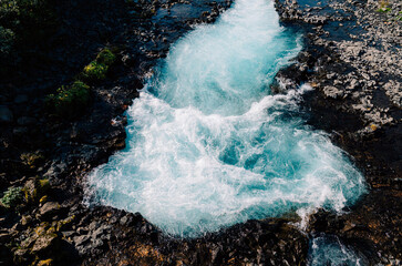 Powerful turquoise river rushes through dark rocks in a close view of foaming rapids, creating a dynamic natural scene ideal for water, wilderness and adventure themes. © UQink