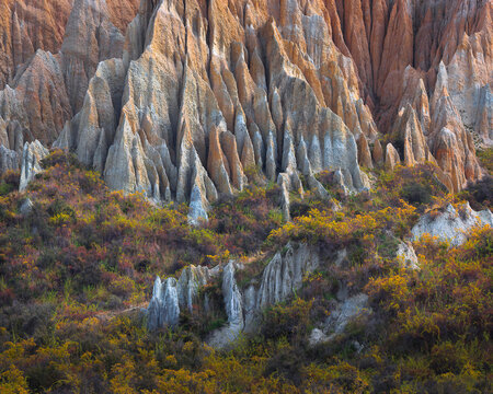 Layered eroded rock spires rise above colorful vegetation, creating a rugged geological landscape ideal for nature, travel, erosion and dramatic terrain themes.