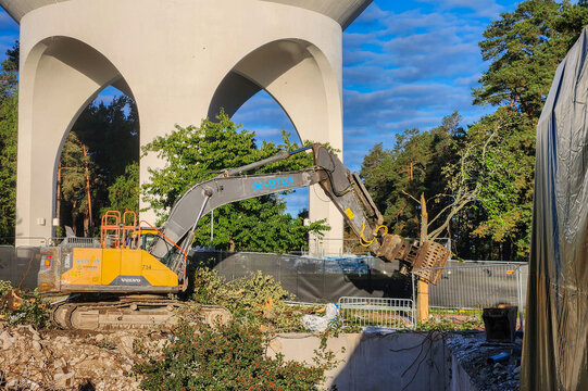 Close up view of Volvo excavator clearing tree beside arched building at construction site. Sweden. Stockholm.