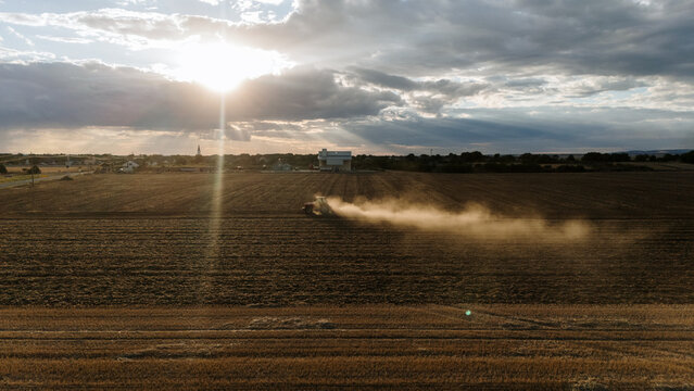 Aerial view of a tractor plowing a field and kicking up dust during golden hour in the rural landscape of Veliki Radinci, Vojvodina, Serbia.