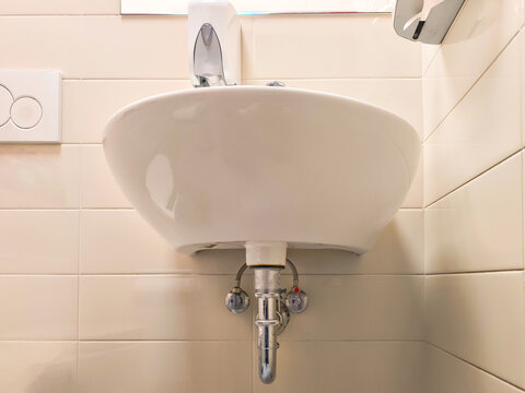 Wall-mounted bathroom sink with soap dispenser and tiled wall. Handwashing hygiene and sanitation. Bathroom fixture and plumbing installation. Restroom hygiene