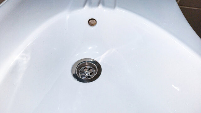 White ceramic bathroom sink basin with metal drain and overflow opening. Close-up view of washbasin plumbing fixture. Bathroom hygiene and handwashing. Residential plumbing and sanitation