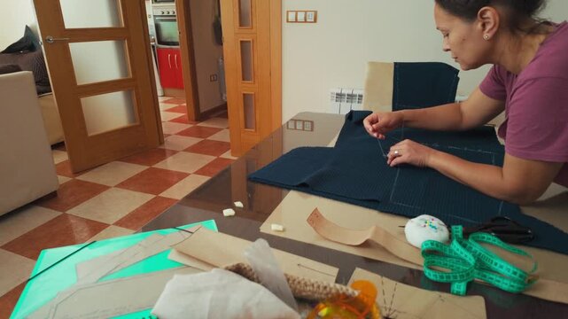 Focused Woman Marks Fabric with Chalk for a Sewing Project at Home, Showcasing Her Craft and Attention to Detail.
