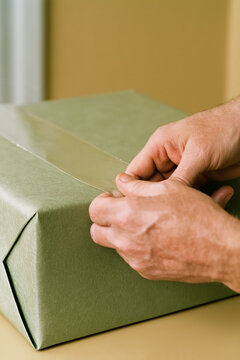 Close up of courier male hands wrapping cardboard parcel box for shipment delivery service, logistics packaging process in post warehouse room with copy space for post order tracking concept