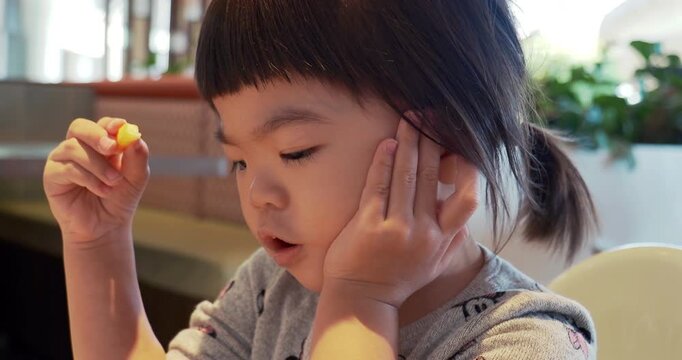 Young Asian toddler girl eating at a fast-food restaurant, hand near her mouth.