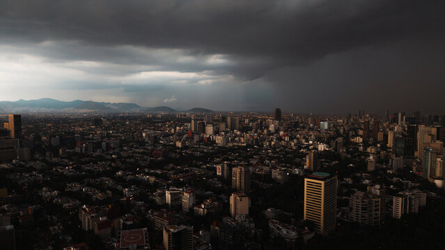 Aerial view of the sprawling Mexico City skyline under dramatic dark storm clouds with high-rise buildings and distant mountains in Mexico City, Mexico City, Mexico.