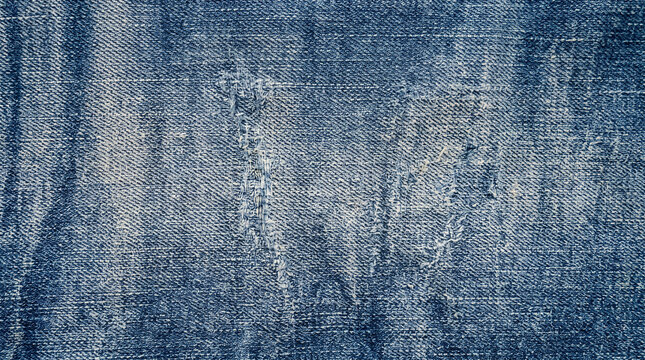 Worn blue denim jeans texture with rips and faded areas, close up of classic fabric for fashion background or textile design concept