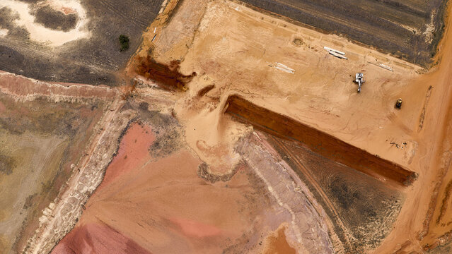 Aerial view of an industrial mining site with deep excavation pits, exposed red earth, sand dunes, and heavy machinery in the remote landscape of Kalbarri, Western Australia, Australia.