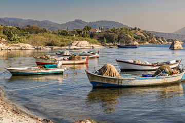 Wooden fishing boats anchored in a calm sea bay with green mountains in background © ufukerb