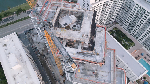 Aerial view of a high-rise building under construction featuring a large yellow tower crane and concrete framework in the urban landscape of Miami Beach, Florida, United States.