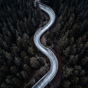 top view of winding bobsleigh track among dense dark green pine forest winter sports complex curved concrete channel for luge and skeleton bird eye view
