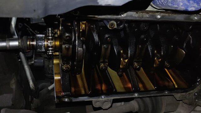 Under-car view of an open engine crankcase showing the oily crankshaft, counterweights, connecting rod caps, and internal mechanical components.