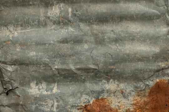 Weathered corrugated metal panel with a dull grey surface, scratches, dents and prominent dark orange and brown rust along the bottom edge. Industrial grunge texture with aged metallic surface and dis