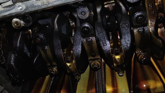Under-car view of an open engine crankcase showing the oily crankshaft, counterweights, connecting rod caps, and internal mechanical components.