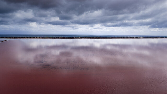 Aerial view of the pink salt lake with reflective clouds and dark storm clouds above in Kalbarri, Western Australia, Australia.